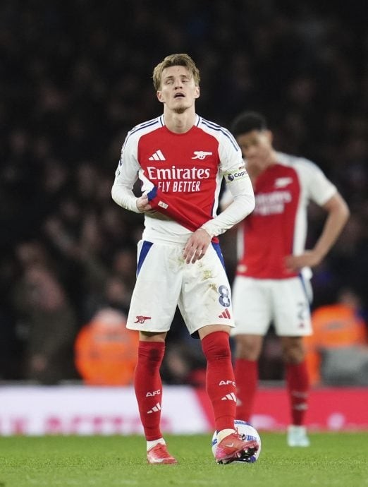 Arsenal captain Martin Ødegaard looks frustrated during a UEFA Champions League match, standing over the ball with hands on his stomach.