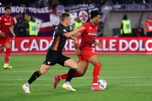 A Fiorentina player dribbles the ball while being closely pursued by a Venezia player during a Serie A match.