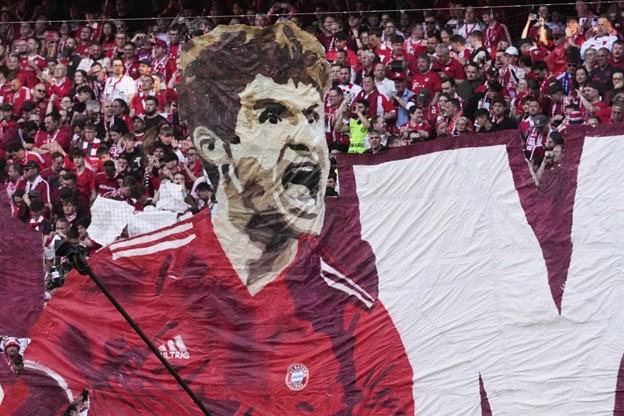Bayern fans unveil a massive banner featuring a roaring illustration of Thomas Müller in a red Bayern jersey, creating an electrifying atmosphere in the stadium.