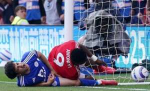 Nottingham Forest forward Taiwo Awoniyi lies injured on the ground after a heavy collision with the goalpost during a Premier League match against Leicester City, as a Leicester player also appears hurt nearby.
